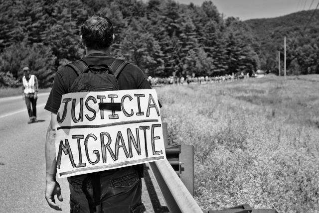 Marching for dignity, a migrant justice supporter proudly displays his support to passing motorists on Route 2 in Middlesex, VT.