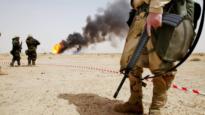 American troops stand next to a burning oil well at the Rumayla oil fields March 27, 2003 in Rumayla, Iraq. (Photo by Mario Tama/Getty Images)