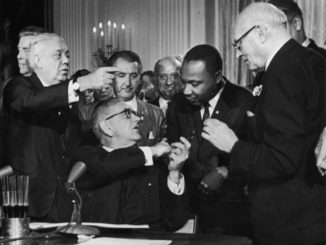US President Lyndon B. Johnson shakes the hand of Dr. Martin Luther King Jr. (1929 - 1968) at the signing of the Civil Rights Act while officials look on, Washington DC. (Photo by Hulton Archive/Getty Images)