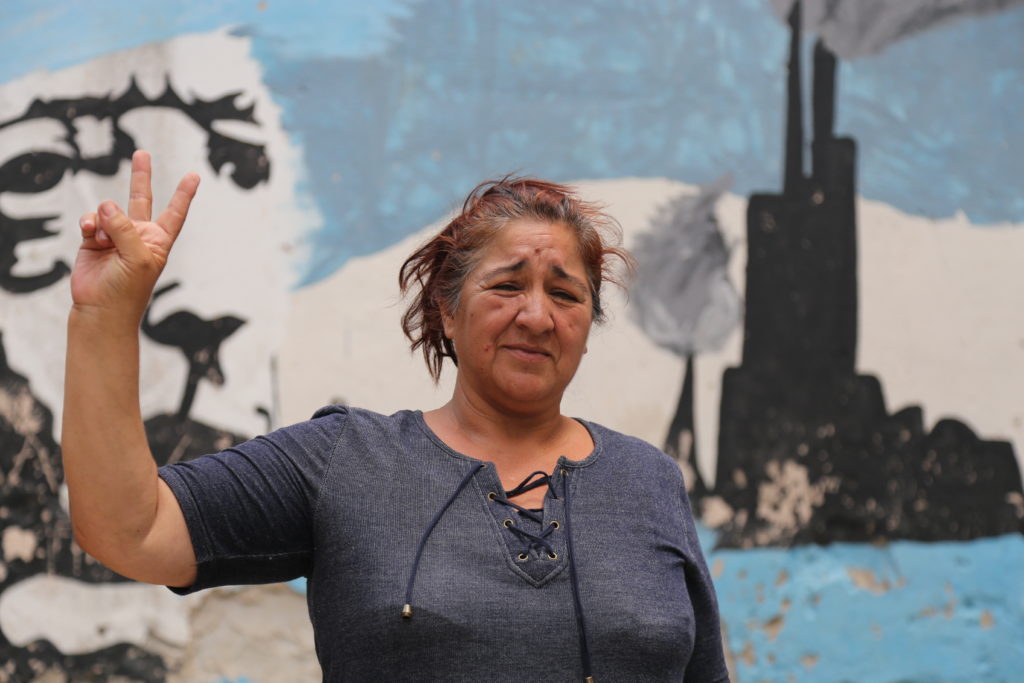 Sandra Garcia stands before a mural of former president Nestor Kirchner and the refinery that overshadows the neighborhood of Dock Sud. Photo by Michael Fox