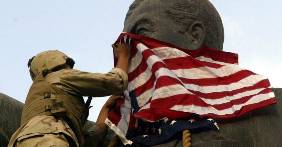 A U.S. Marine covers the face of a statue of Iraqi President Saddam Hussein with a U.S. flag in Baghdad, on April 9, 2003. (Photo: AP)