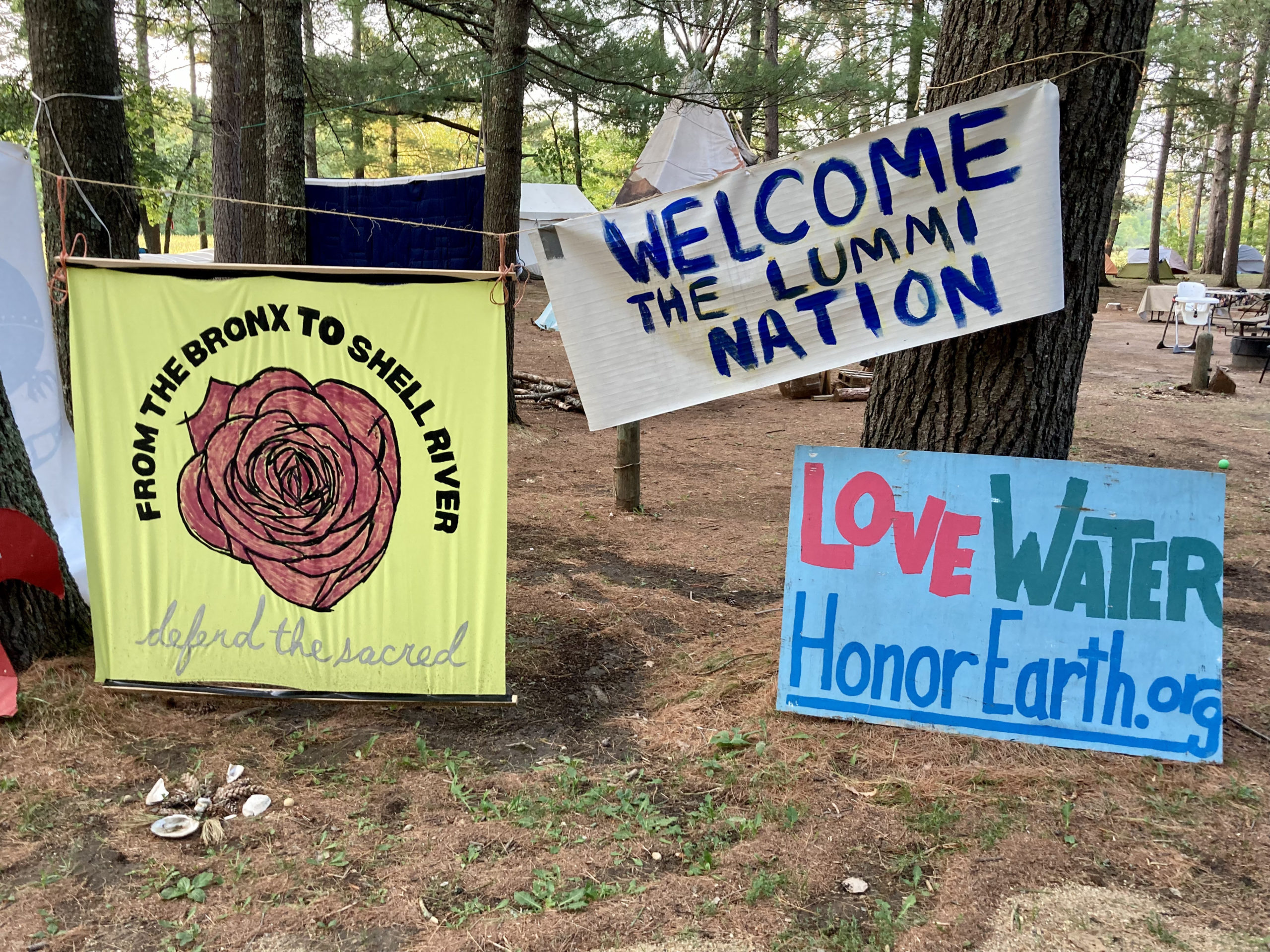 Signs at the camp read, from left to right, “From the Bronx to Shell River: Defend the Sacred,” “Welcome the Lummi Nation” and “Love Water: HonorEarth.org”