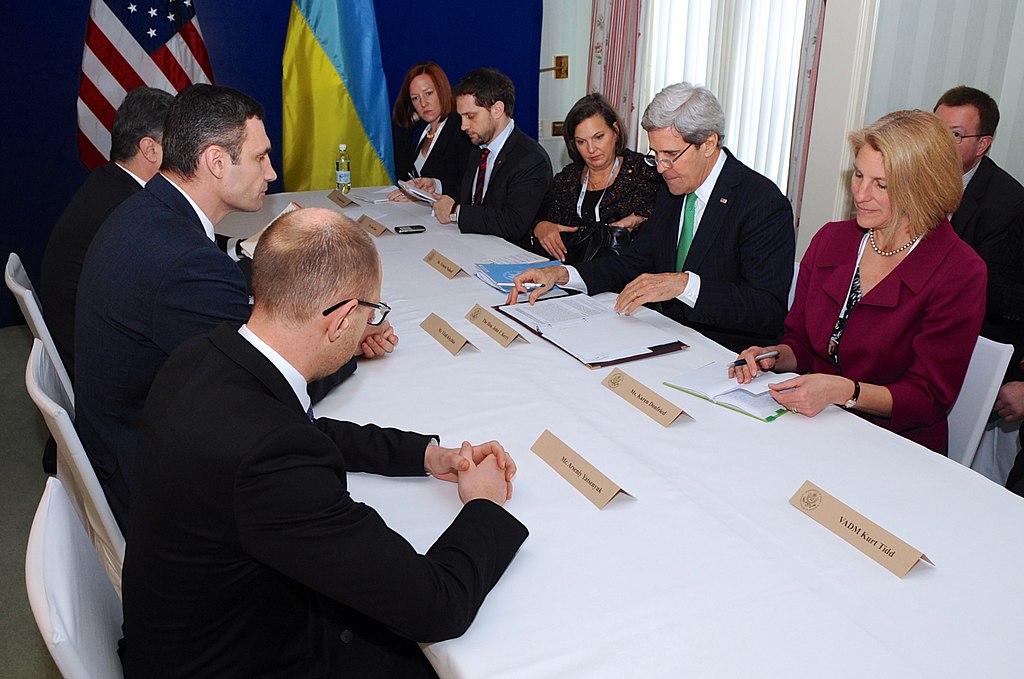 U.S. Secretary of State John Kerry and his team sit across from Petro Poroshenko of the Euromaidan Movement, Vitali Klychko of the UDAR Party, and Arseniy Yatsenyuk of the Fatherland Party at the outset of a meeting with the Ukrainian opposition leaders on the sidelines of the Munich Security Conference in Munich, Germany, on February 1, 2014. Victoria Nuland can be seen to Kerry's right (fourth from the right) / credit: U.S. State Department