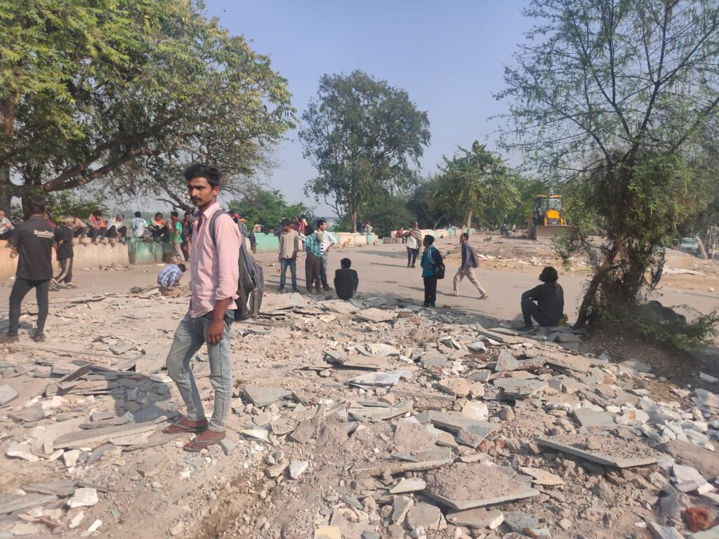 Yamuna Pushta resident Rohit Sharma (standing, in a pink shirt) on the spot where his bed once lay before a night shelter was demolished / credit: Parva Dubey
